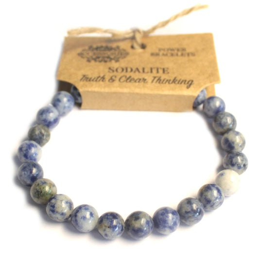 A blue and white beaded bracelet encircles a kraft paper tag reading "Sodalite, Truth & Clear Thinking, POWER BRACELETS". A twine string is attached to the tag, over a white surface.