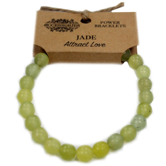 A jade bracelet is arranged on a white background. It's held by a brown cardboard tag that says “ACCESSORIES,” “POWER BRACELETS,” and “JADE Attract Love”.