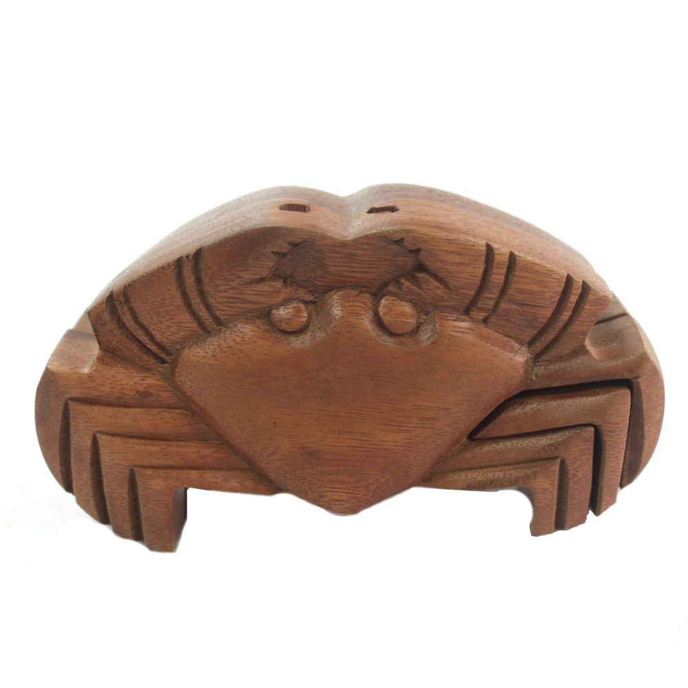 A wooden sculpture of a crab resting on a flat surface, featuring intricately carved details on the shell and legs, in a simple, light-colored environment.