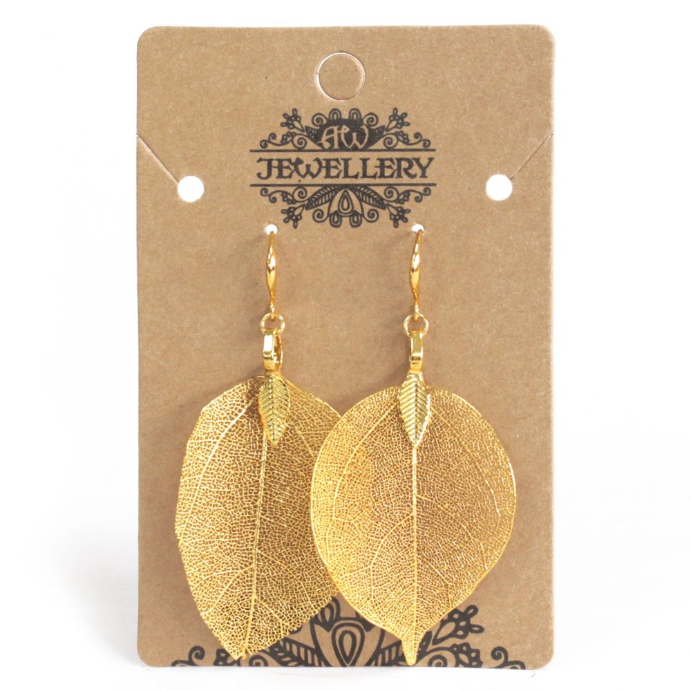 A pair of gold leaf earrings hangs from a brown cardboard display. The card is labeled “AW JEWELLERY.”