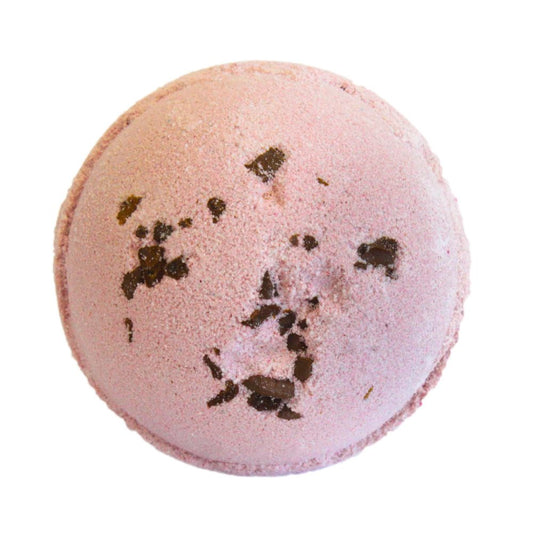 Pink bath bomb with dark specks resting atop, against a plain white background.