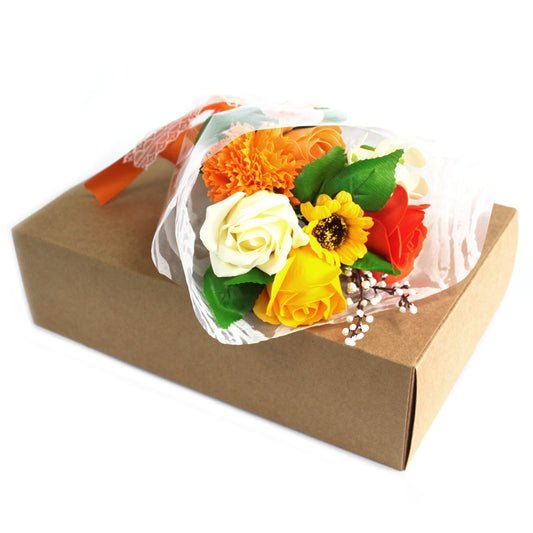 Bouquet of mixed roses and a sunflower rests wrapped in translucent paper atop a closed brown cardboard gift box on a white background.