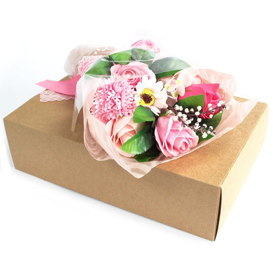Bouquet of pink roses and mixed flowers rests on a closed brown cardboard gift box on a white background.