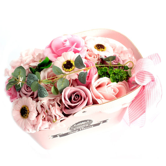 Heart-shaped pink box holds an arrangement of pink artificial roses, daisies and eucalyptus sprigs on a white background with a pink gingham bow; label reads "Soap Flowers".