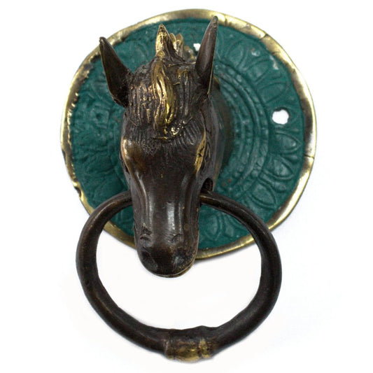 A bronze horse head forms a door knocker; it is mounted on a teal circular plate.