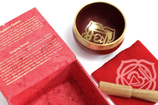 A red singing bowl set includes a decorative bowl and wooden striker, accompanied by a red mat. The open red box displays text about chakras and singing bowls.