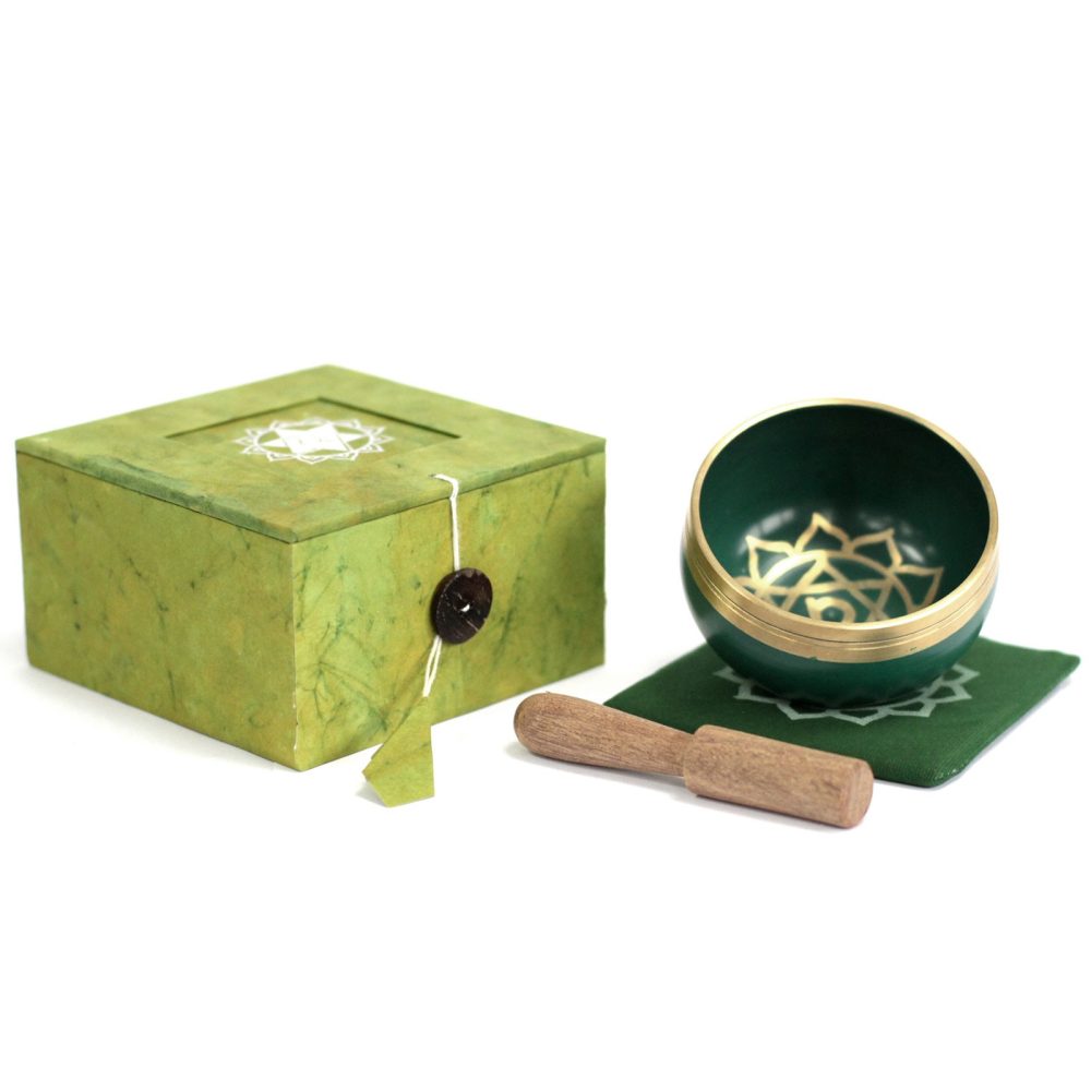 A green singing bowl with intricate patterns rests on a matching mat beside a wooden striker. A decorative green box with a symbol on its lid completes the set.