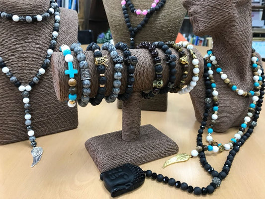 Necklaces and bracelets are displayed on brown stands, featuring stones like black lava, agate, and turquoise on a light wood surface.