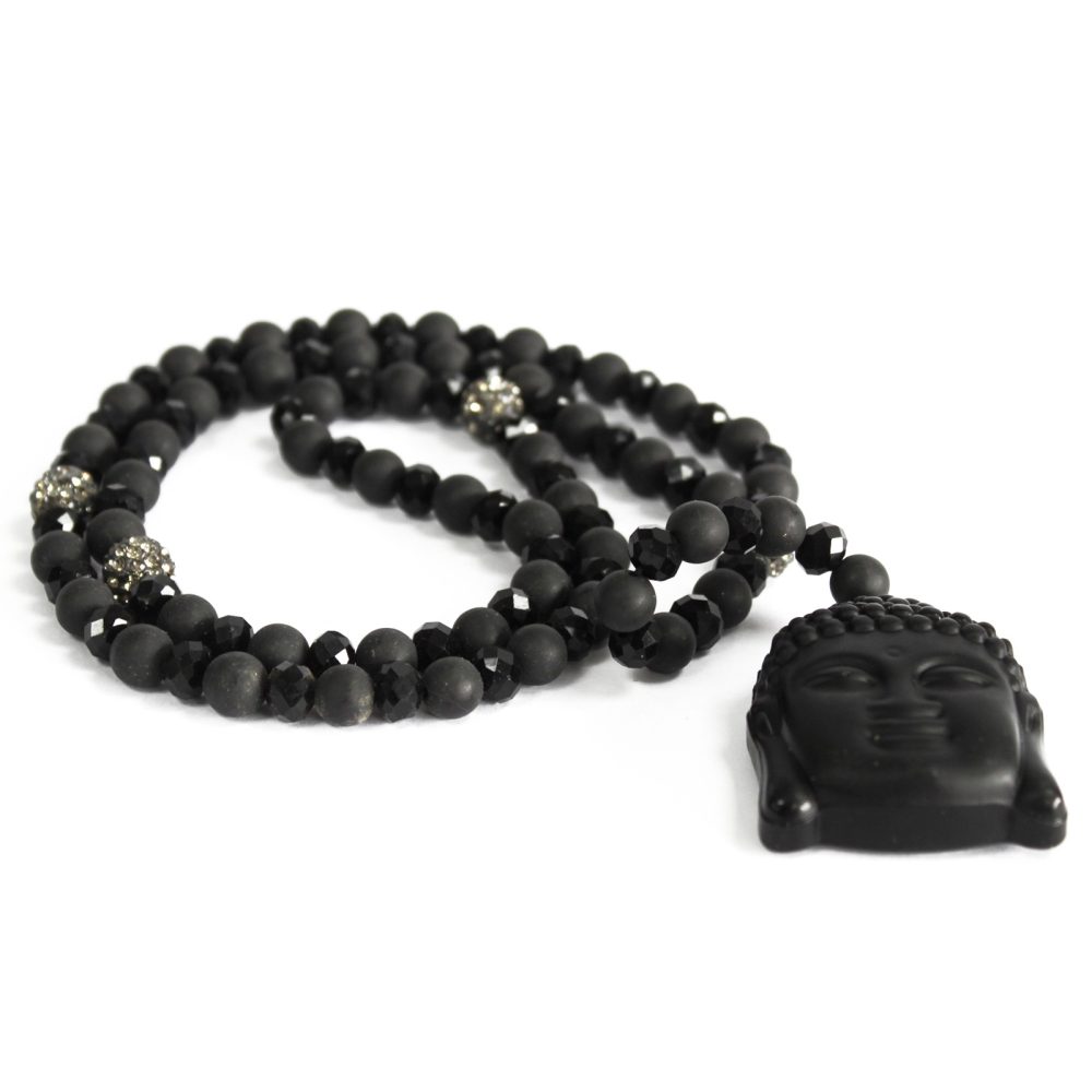 A black bead necklace, featuring a Buddha pendant, is laid out on a white surface. Some of the beads are matte, and some are shiny and faceted. There are also some silver, pave-style beads.