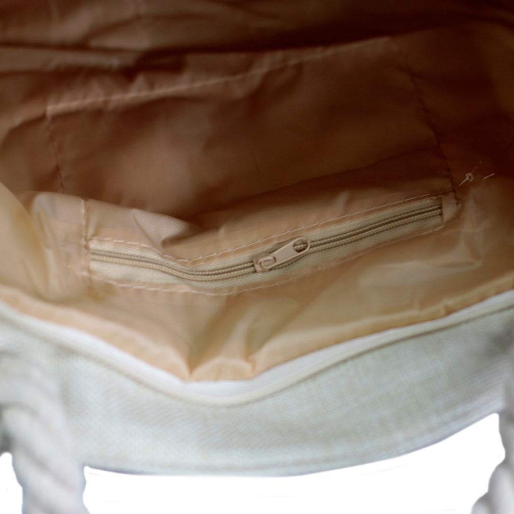 The interior of a beige tote bag is visible, featuring a zippered pocket against the back, light-beige lining, and rope handles in the lower corners.