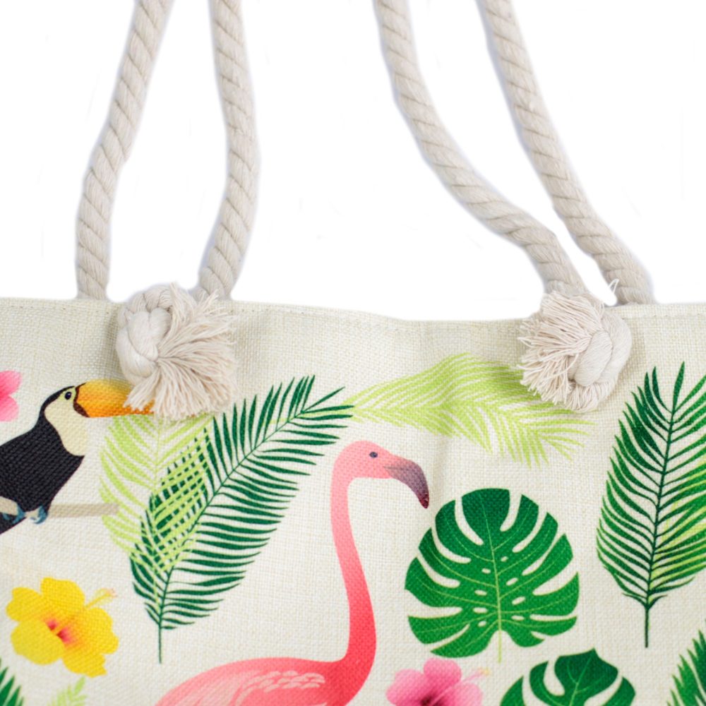 A canvas tote bag features a pattern of tropical foliage, flamingoes, toucans, and flowers. The bag has thick rope handles knotted at the top.