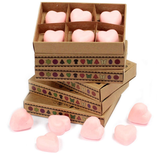 Heart-shaped wax melts are stacked in cardboard boxes, decorated with small, colorful designs. Several additional melts sit scattered on a white surface.
