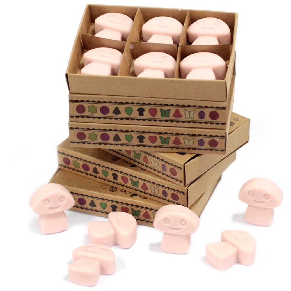 Pink mushroom-shaped wax melts are packaged in stacked cardboard boxes with whimsical designs.  Several additional melts sit scattered nearby.