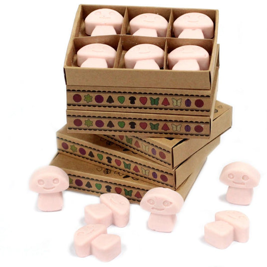 Pink mushroom-shaped wax melts are packaged in a stack of decorated cardboard boxes.  Several additional melts are scattered nearby on a white surface.