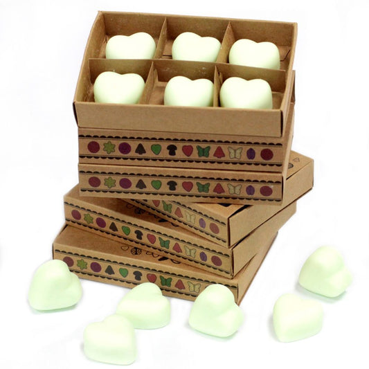 Heart-shaped wax melts are stacked in cardboard boxes decorated with a repeating pattern of small icons. Several additional melts are scattered nearby on a white surface.