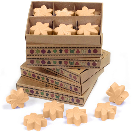Flower-shaped wax melts are stacked in decorated boxes.  Several additional melts are scattered nearby.
