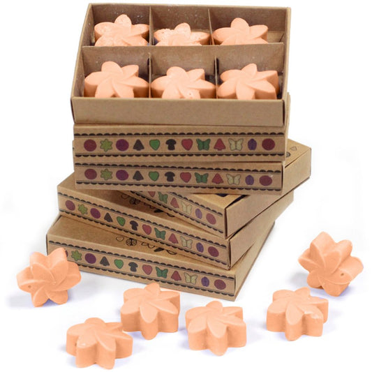 Peach-colored wax melts, arranged in a box and scattered nearby, sit on a white surface. The boxes are brown cardboard with a repeating decorative border.