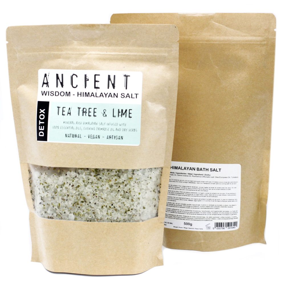 Two kraft bags stand, one slightly behind the other. The front bag has a clear window showcasing white and green bath salts; it’s labeled "ANCIENT", "WISDOM - HIMALAYAN SALT," "DETOX," "TEA TREE & LIME", and details ingredients. The rear bag displays "HIMALAYAN BATH SALT" and some ingredient info. "500g" and a barcode appear on its lower section.