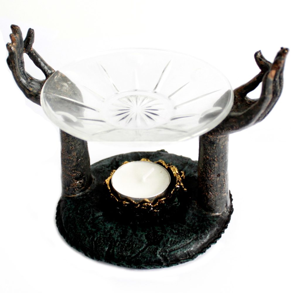 A glass dish held by two metallic hands above a decorative stand with a tealight candle in a golden holder, creating an artistic and serene display piece.