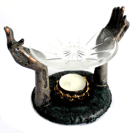 Two sculpted hands hold a glass dish above a small candle holder. The setup is on a textured circular base, with a decorative and artistic appearance.