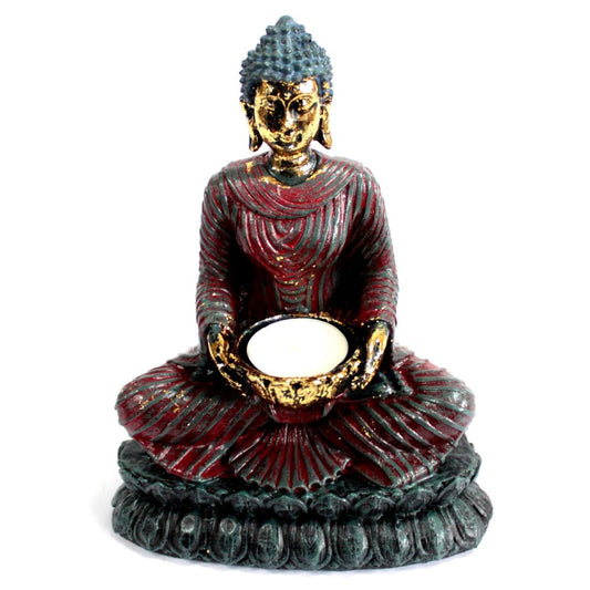 Buddha statue sits cross-legged on a carved lotus pedestal, holding a small gold-rimmed bowl with a white tealight; painted red, gold, and green with blue hair on a white background.