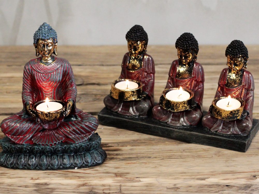 A large red Buddha figure and three smaller Buddhas hold lit tealight candles; all are positioned on a wooden surface, suggesting a serene, decorative setting.
