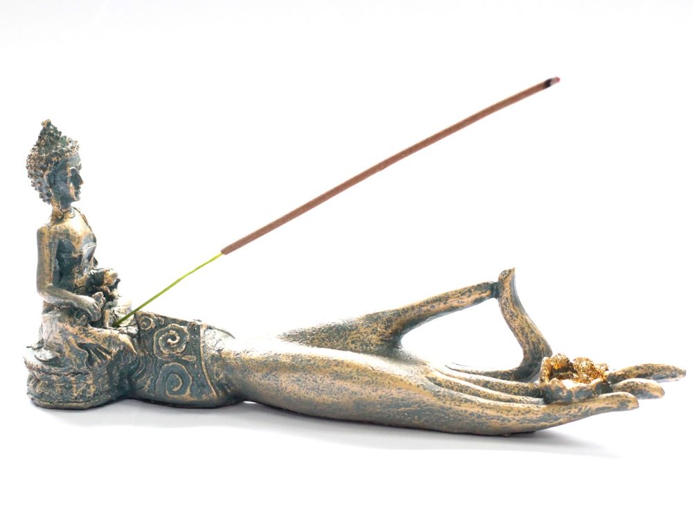 Ornate incense holder features a seated figure positioned on an elongated hand, which grasps golden nuggets. The incense stick rests diagonally, creating a balance between elegance and functionality.