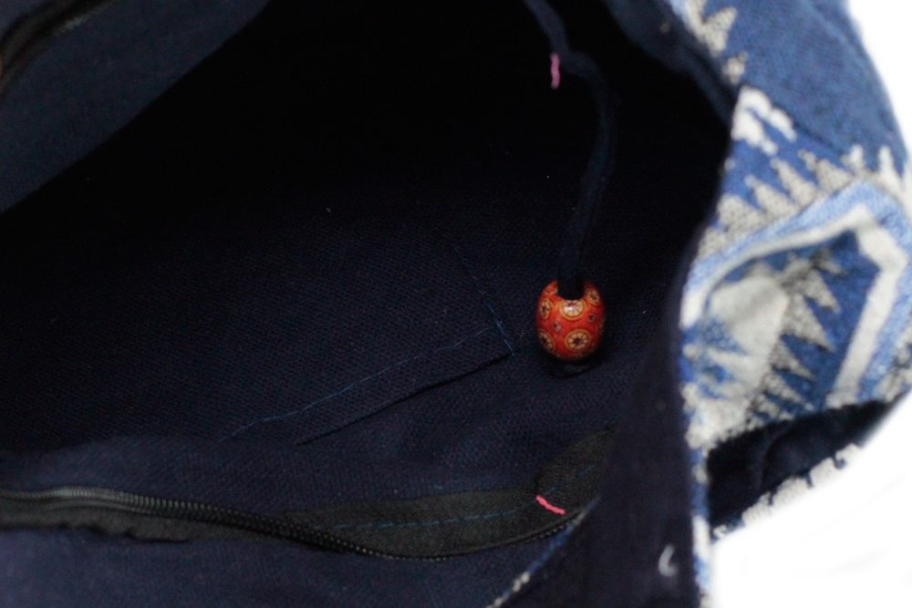A tote bag reveals its dark navy interior with a small pocket and zipper. A decorative orange bead dangles on a string. The bag's patterned blue and white exterior is partially visible.