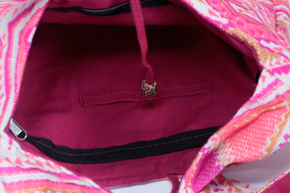 The inside of a brightly colored bag is shown, revealing a deep magenta lining and a small pocket. A drawstring with a decorative bead hangs down.