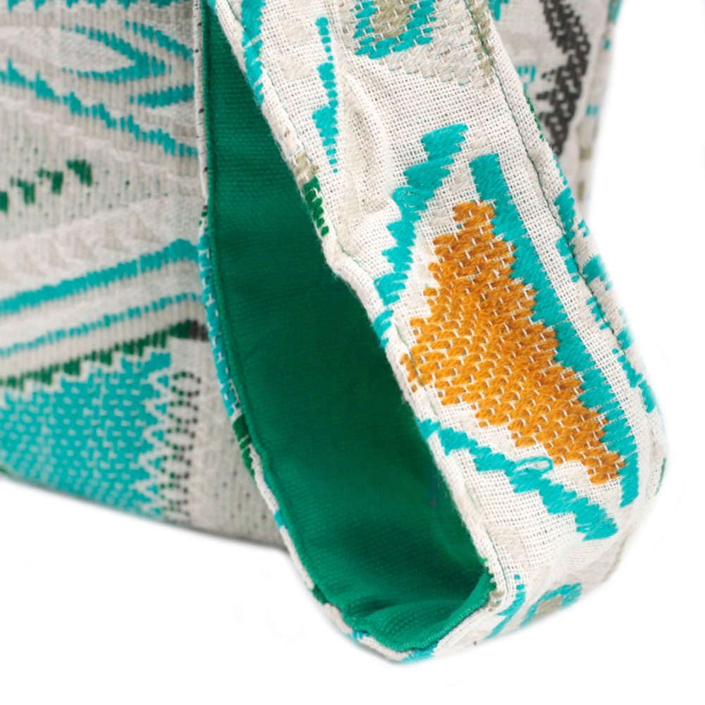 A fabric bag displays its handle, revealing a smooth, green interior. The exterior features a woven pattern of geometric shapes in colors like teal, brown, and gray against an off-white background.