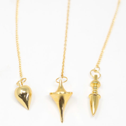 Three golden pendulums, heart-shaped, conical, and spindle-shaped, hang suspended by delicate golden chains against a stark white background.