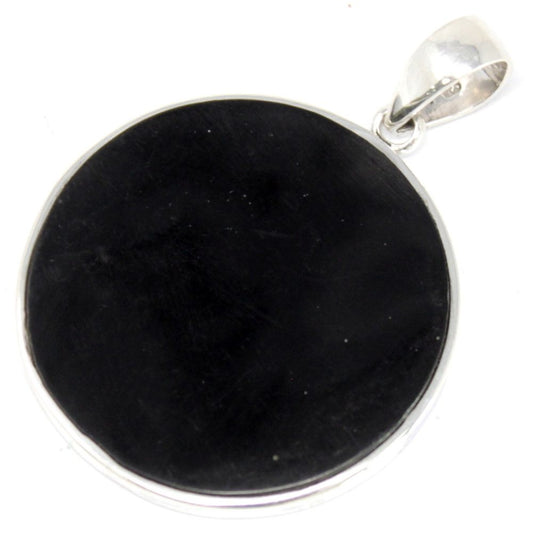 A round black stone pendant rests on a white surface. The pendant is encased in silver and includes a silver loop for hanging.