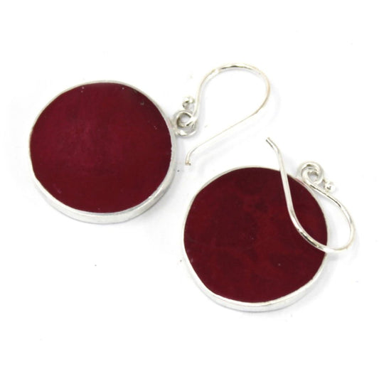 Two circular, deep red earrings with silver rims and hooks rest against a clean, white surface.