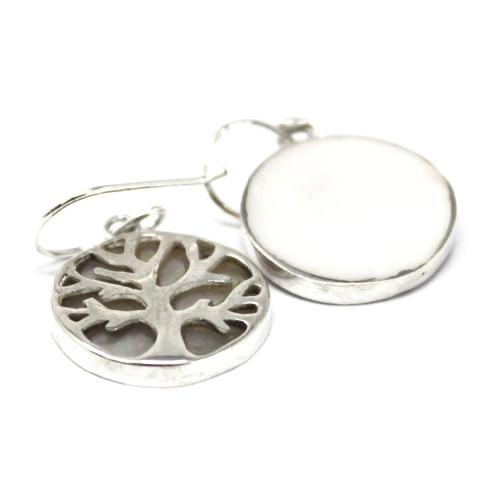 Two silver earrings dangle: one with a tree-shaped cutout, the other a solid white disc, both with silver borders, shown on a white background.