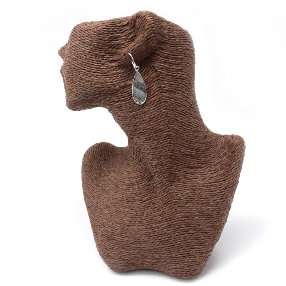A teardrop earring hangs from the ear of a brown, woven mannequin head and neck set against a stark white background.