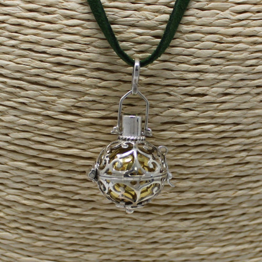 A silver, filigree sphere, suspended from a green cord, hangs against a textured, woven, light-brown surface. The sphere appears to open, revealing a gold-colored interior.