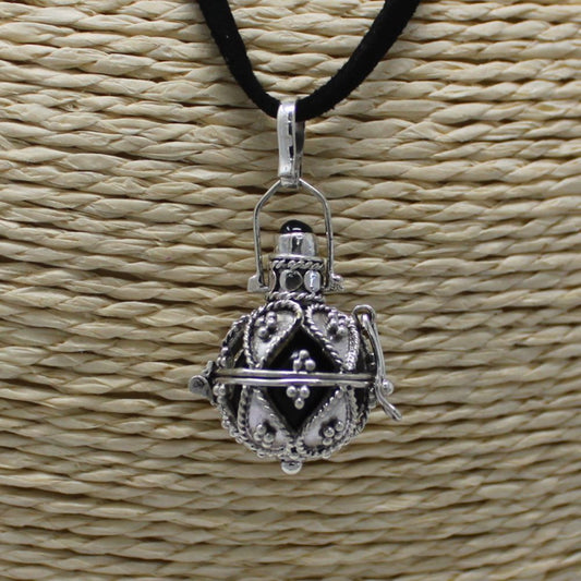 A silver ball pendant hangs from a black cord. The pendant rests against a textured beige woven background.