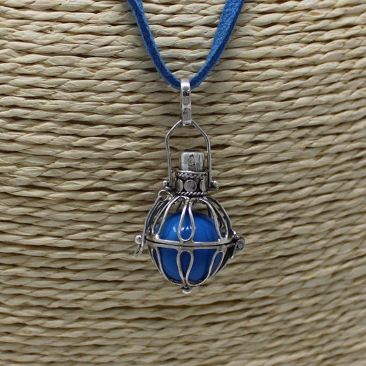 A necklace with a silver cage pendant holding a blue, spherical stone hangs against a textured beige background. The necklace has a blue suede cord.