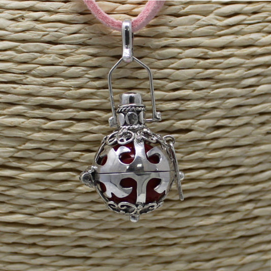 A silver filigree orb pendant hangs from a pink cord. The orb is against a background that looks like woven straw.