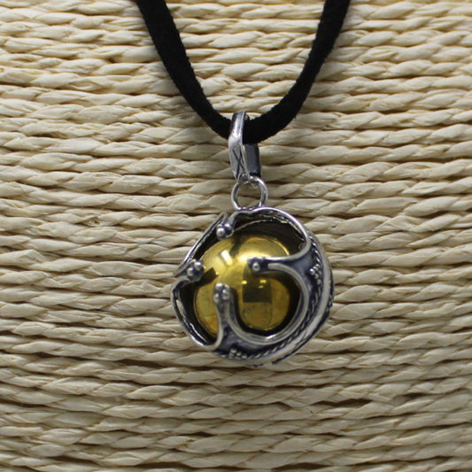A golden sphere, enclosed in a silver filigree cage, hangs from a black velvet cord. It rests against a woven, light-tan background.