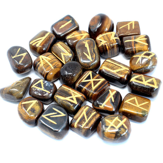 Polished, brown tiger's eye stones sit in a scattered pile. Each stone displays a yellow rune symbol etched on its surface against a white backdrop.