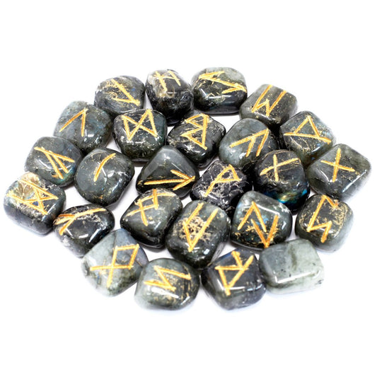 Rune stones are scattered across a white surface. The stones are dark grey with gold symbols etched on each one.