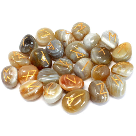 Polished stones with golden, rune-like symbols are scattered on a white surface. The stones are various shades of brown, white, and gray.
