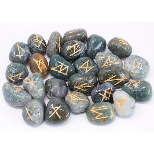 Polished stones, each engraved with a unique rune, scatter across a white surface. The stones vary in shades of green, gray, and brown.