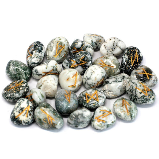 A pile of polished rocks, each adorned with golden runic symbols, scatters on a white surface. The stones vary in color and texture, ranging from green and gray to white and black with marbled patterns.