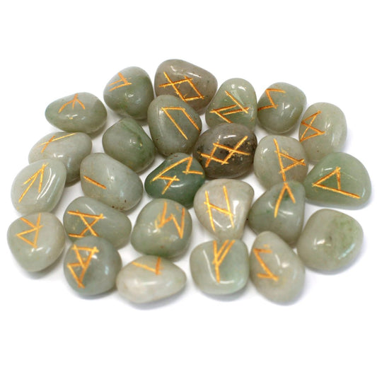 Pale green polished stones are strewn across a white surface, each bearing a unique, stylized golden sigil on its face.