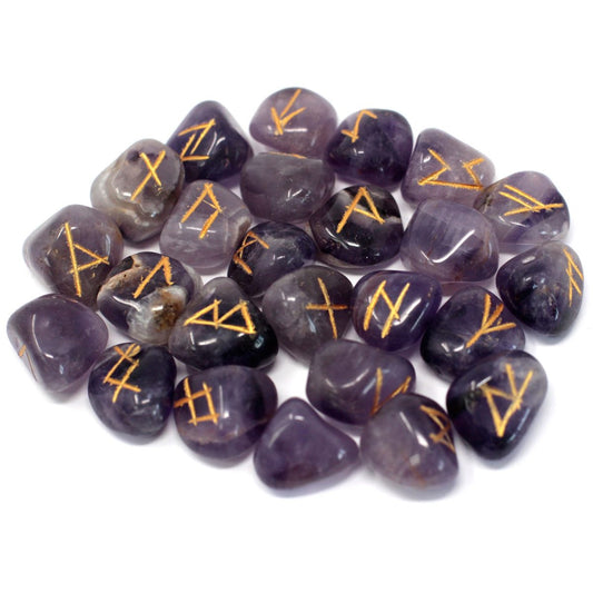 Pile of polished purple stones show gold-colored symbols etched on their surfaces, arranged on a white background.