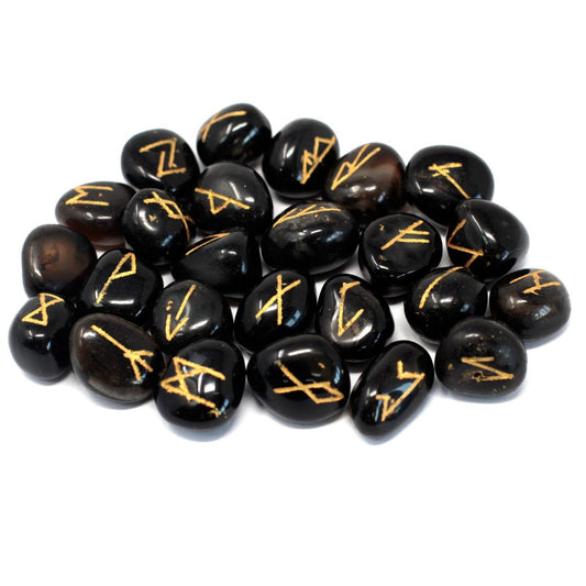Several dark, shiny stones display gold rune symbols, scattered randomly on a plain white surface.
