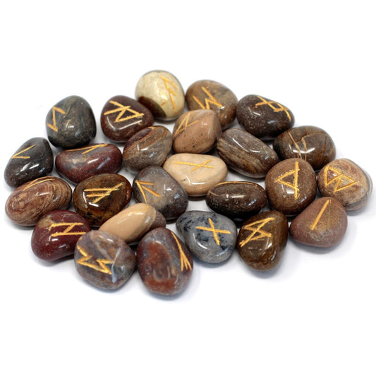 Rune stones are arranged in a pile on a white surface. The smooth, polished stones are various shades of brown, beige, and gray, each etched with a golden rune symbol.