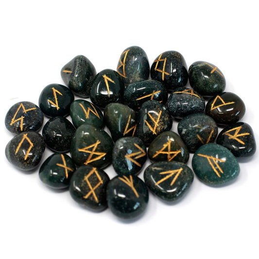 Smooth, green stones with etched gold symbols are scattered against a white background. The stones are various sizes and shapes and seem to be rune stones.